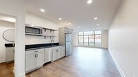 Located in the heart of Lancaster, PA, Suite 411 at 8 W King Street is a thoughtfully designed space that blends contemporary finishes with a clean, minimal aesthetic. The unit spans a single floor and comprises five rooms, offering a well-organized and functional layout.

The open-plan kitchen and living area serves as the centerpiece of the space. The kitchen is outfitted with white shaker-style cabinetry, dark countertops, stainless steel appliances including a refrigerator, dishwasher, and microwave, as well as open floating shelves — delivering both style and practicality. This area flows seamlessly into a bright, spacious living zone illuminated by large floor-to-ceiling windows that frame views of Lancaster's historic downtown rooftops and architecture.

Light wood-look flooring extends throughout the space, complementing the crisp white walls and recessed lighting found in every room. A long, well-lit corridor connects the main living area to the additional rooms, which are bright and versatile. The bathroom features a frameless glass walk-in shower with elegant marble-style tile surround and matching cabinetry with dark countertops.

The abundant natural light, modern finishes, and urban views make this a polished and inviting space in the heart of downtown Lancaster.