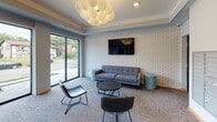Located at 333 SE Eighth St in Minneapolis, Minnesota, this building lobby offers a well-appointed, single-floor communal space designed to welcome residents and visitors alike. The layout balances functionality with a contemporary aesthetic, creating an inviting atmosphere from the moment you enter.

The entry area features a glass-paneled door with a dark metal frame, providing a clear sightline into the lobby. A package locker system and resident mailboxes are conveniently positioned near the entrance, offering practical amenities in an accessible location. An elevator provides vertical access to the building's upper floors.

The lounge area is the focal point of the space, anchored by a gray tufted sofa, leather accent chairs, and a round coffee table arranged on patterned carpeting. A large flat-screen television is mounted on a textured white brick accent wall, adding visual character and a comfortable, communal feel. Teal side tables introduce a subtle pop of color throughout the seating area.

Floor-to-ceiling windows along one wall flood the space with natural light and frame views of the surrounding Minneapolis neighborhood. Overhead, a sculptural globe chandelier composed of clustered spheres serves as a striking design centerpiece. Tray ceiling detailing further enhances the polished, modern ambiance of the lobby.