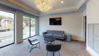 Located at 333 SE Eighth St in Minneapolis, Minnesota, this building lobby offers a well-appointed, single-floor communal space designed to welcome residents and visitors alike. The layout balances functionality with a contemporary aesthetic, creating an inviting atmosphere from the moment you enter.

The entry area features a glass-paneled door with a dark metal frame, providing a clear sightline into the lobby. A package locker system and resident mailboxes are conveniently positioned near the entrance, offering practical amenities in an accessible location. An elevator provides vertical access to the building's upper floors.

The lounge area is the focal point of the space, anchored by a gray tufted sofa, leather accent chairs, and a round coffee table arranged on patterned carpeting. A large flat-screen television is mounted on a textured white brick accent wall, adding visual character and a comfortable, communal feel. Teal side tables introduce a subtle pop of color throughout the seating area.

Floor-to-ceiling windows along one wall flood the space with natural light and frame views of the surrounding Minneapolis neighborhood. Overhead, a sculptural globe chandelier composed of clustered spheres serves as a striking design centerpiece. Tray ceiling detailing further enhances the polished, modern ambiance of the lobby.