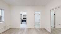 Located at 1310 S Wilton Pl in Los Angeles, CA, this efficiently designed one-bedroom, one-bathroom unit offers a clean, modern aesthetic with thoughtful updates throughout. The interior is finished in a bright white palette, creating an open and airy feel despite its compact footprint.

The living area flows directly into the kitchen and bedroom, making efficient use of the available space. Light wood-tone laminate flooring runs through the main living and bedroom areas, lending warmth to the otherwise crisp, white interior. A window unit provides climate control in the bedroom, which also features a full-width mirrored sliding closet door that reflects light and adds a sense of depth to the room. A second closet offers additional storage.

The kitchen is a standout feature, equipped with stainless steel appliances including a full-size refrigerator, a gas range with overhead ventilation, and ample white shaker cabinetry with black hardware. Marble-style tile flooring completes the polished look of this functional cooking space.

The bathroom is clean and simple, featuring a shower-tub combination, a pedestal sink, and black accent hardware consistent with the unit's modern styling. The all-white finishes keep the space feeling fresh and well-maintained. Overall, this unit provides a practical and attractively updated living space in a central Los Angeles location.