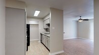 Located at 6803 N Navarro St in Victoria, Texas, this single-floor unit offers a functional and well-appointed layout throughout. The living area features warm wood-look laminate flooring, neutral-toned walls, and a ceiling fan with integrated lighting. Vertical blinds cover a sliding glass door that allows natural light to fill the space. The open pass-through connects the living area to the kitchen, enhancing the sense of flow between rooms. The galley-style kitchen is efficiently designed with gray shaker-style cabinetry, granite-look countertops, a mosaic tile backsplash, and black appliances including a refrigerator, range, and built-in microwave. A stainless steel sink and dishwasher complete the kitchen's practical features, with a skylight-style ceiling fixture providing overhead illumination. The bedrooms are finished with plush carpet flooring, ceiling fans, and windows with blinds that bring in natural light. One bedroom includes access to a walk-in closet and a private en-suite bathroom. The bathroom is finished with large-format gray tile, a granite-topped vanity with gray cabinetry, a soaking tub, and a well-lit mirror. Throughout the unit, consistent neutral tones and clean finishes create a cohesive and move-in-ready environment.