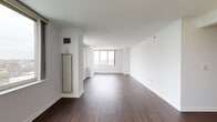 Located at 1 City Place in White Plains, NY, this single-floor residence offers a clean, modern aesthetic defined by crisp white walls, crown molding, and rich dark hardwood flooring throughout the main living areas. The expansive living room is bathed in natural light from multiple large windows that frame elevated views of the White Plains skyline, creating an open and airy atmosphere. A decorative wall sconce accents the entry hallway, which leads seamlessly into the main living spaces.

The kitchen is equipped with stainless steel appliances, including an electric range and over-the-range microwave, and features light tile flooring and ample counter space. The bathrooms are finished with warm travertine-style tile, with one bathroom offering a full soaking tub and shower combination with brushed nickel fixtures, and another featuring a classic pedestal sink, oval mirror, and tile flooring. Bedrooms are generously sized with large windows overlooking the city. A dedicated in-unit laundry closet houses a full-sized washer and dryer with overhead shelving, adding everyday convenience to this well-appointed urban residence.