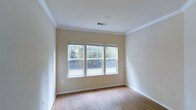 This single-floor space presents a clean, well-maintained interior defined by its warm, neutral palette and thoughtful architectural details. The room is finished with smooth hardwood-style flooring in a light wood tone, contributing to a bright and welcoming atmosphere throughout. Crown molding lines the perimeter where the walls meet the ceiling, adding a refined touch to the otherwise understated design.

A trio of double-hung windows positioned along one wall serves as a central feature of the space, drawing in generous amounts of natural light and providing pleasant views of surrounding greenery and trees. The windows are fitted with horizontal blinds, offering flexible light control while maintaining a tidy appearance.

The walls are painted in a soft, warm beige tone that complements the flooring and enhances the overall sense of openness. Crisp white baseboards and window trim provide clean contrast throughout the room. A ceiling-mounted HVAC vent ensures efficient climate control, and an electrical outlet is conveniently placed along the wall. The overall ambiance is light, airy, and move-in ready, offering a versatile blank canvas suitable for a variety of uses.