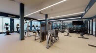 Located at 1631 Paterson Plank Rd in Secaucus, NJ, this fitness center is a thoughtfully designed, single-floor facility that offers a comprehensive workout environment. The space is organized into distinct zones, each tailored to specific training needs. The main workout floor features durable speckled rubber flooring and is lined with a row of treadmills and cardio equipment positioned along floor-to-ceiling windows, allowing natural light to fill the space and providing views of the surrounding area. Ceiling fans and linear LED lighting run overhead, contributing to a clean, well-lit atmosphere.

The strength training area is equipped with cable machines, weight racks, a full dumbbell selection, and benches, all arranged to maximize open floor space. Large mirrors along the walls enhance the sense of depth and allow users to monitor their form. A dedicated training zone features TRX suspension equipment, kettlebells, and resistance tools, signaled by prominent wall signage.

A separate spin studio with glass door entry houses stationary cycling bikes on light wood flooring, accented by large windows and mirrored walls. Safety amenities, including a wall-mounted AED unit, a water fountain station, and glass-panel entry doors, are also present throughout the facility.