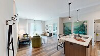 This thoughtfully designed 2-bedroom, 2-bathroom residence spans a single floor and delivers a modern, open-concept living experience. Wood-style plank flooring flows throughout the main living areas, creating a warm and cohesive aesthetic. The kitchen is a standout feature, showcasing dark wood cabinetry paired with crisp white upper cabinets, a subway tile backsplash, stainless steel appliances, a large undermount sink, and a center island with quartz countertops and pendant lighting — ideal for both cooking and casual dining. The kitchen opens seamlessly into the living and dining areas, which are bright and airy, benefiting from generous natural light and sliding glass door access to an outdoor balcony. The primary bedroom is a comfortable retreat with plush carpet, a dedicated closet, and a private en-suite bathroom featuring a wide vanity with modern fixtures and cage-style lighting. The second bedroom is equally well-sized with its own closet and easy access to the second full bathroom. Both bathrooms are finished with contemporary gray cabinetry and clean, neutral tones. Additional spaces include a hallway, utility room, and closet, ensuring ample storage throughout. The overall ambiance is modern, bright, and functional.