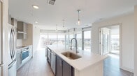 Located at 10 Westedge St in Charleston, SC, this modern 4-bedroom, 2-bathroom residence offers an elevated living experience with sweeping views of the city's waterways and skyline. Floor-to-ceiling glass windows and sliding doors flood the open-plan living areas with abundant natural light, framing breathtaking panoramic vistas that stretch across Charleston's scenic harbor and surrounding landscape.

The kitchen serves as a central showpiece, anchored by an expansive quartz waterfall island with an integrated sink and a sleek pull-down faucet. Pendant lighting hangs above the island, complementing the gray shaker cabinetry, white tile backsplash, stainless steel appliances, and a professional-grade range hood. Wood-look flooring runs throughout the main living areas, adding warmth to the contemporary design.

The primary bedroom is generously proportioned, featuring wraparound floor-to-ceiling windows with corner views of the waterway and a ceiling fan overhead. The bathrooms are finished with large-format tile flooring, gray vanity cabinetry with quartz countertops, and a glass-enclosed walk-in shower. Additional bedrooms offer clean, light-filled spaces with hardwood-style floors. A dedicated closet and in-unit laundry add further convenience to this well-appointed high-rise residence.