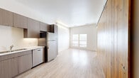 This thoughtfully designed one-bedroom, one-bathroom unit in Denver's 80211 neighborhood offers a modern and efficient layout with contemporary finishes throughout. The open-concept living and kitchen area is anchored by a striking full-height sliding barn door crafted from natural knotty wood, serving as both a functional divider and a bold design statement against the otherwise clean, neutral palette.

The kitchen is well-appointed with sleek, dark wood-grain cabinetry extending to the ceiling, stainless steel appliances including a refrigerator, range, microwave, and dishwasher, and light countertops that complement the overall aesthetic. Light wood-style flooring runs continuously through the main living areas, enhancing the sense of openness and warmth. A double-pane sliding glass door allows natural light to fill the living space.

The bedroom offers a comfortable and private retreat with the same hardwood-style flooring and access to closet storage. The bathroom features large-format marble-style tile flooring, a modern vanity with a white countertop, a full mirror, and clean white walls. A dedicated laundry area includes a stacked washer and dryer for added convenience. A hallway with additional closet space completes this efficiently arranged and stylish Denver residence.