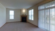 Located at 1910 Hawks Ridge Dr in Verona, Wisconsin, this single-floor home offers a comfortable and well-appointed living environment. The living room serves as the heart of the home, highlighted by a wood-trimmed fireplace that adds warmth and a classic focal point to the space. Plush wall-to-wall carpeting runs throughout, providing a soft underfoot feel and a cohesive aesthetic. Natural light flows generously into the room through multiple windows, including a large double-pane window and vertical blind-covered sliding door or window panel, brightening the neutral, light-toned walls. The open layout of the living area conveys a spacious and airy ambiance, well-suited for both relaxing and entertaining. The understated color palette of warm beige tones throughout creates a calm and inviting atmosphere. Overall, the home presents a clean, move-in-ready interior with functional design elements that balance comfort and practicality, all situated in the established Hawks Ridge neighborhood of Verona, WI.