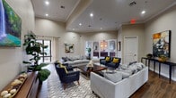 This single-floor clubroom in Spring, TX is a well-appointed community gathering space designed with both comfort and style in mind. The main lounge area features soaring ceilings with recessed lighting and rich hardwood-style flooring throughout. Generously sized gray sectional sofas and dark navy accent chairs, accented with yellow throw pillows, are arranged around a wood-and-gold coffee table atop a patterned area rug. Wall-mounted flat-screen televisions and contemporary abstract artwork contribute to the polished aesthetic. Large windows and glass-panel doors allow natural light to flow in, offering views of the surrounding outdoor amenity areas.

Adjacent to the lounge, a fully equipped catering kitchen stands out with dark espresso cabinetry, a subway tile backsplash, stainless steel appliances, and an expansive marble-topped island with bar seating. A striking metallic ceiling and geometric pendant lights lend this area a sophisticated, upscale character.

A separate game room features dramatic arched windows framing outdoor views, exposed dark ceiling beams, and a billiards table, creating a relaxed yet refined atmosphere. Additional rooms visible from the main lounge appear to serve as private workspaces or meeting areas, completing this versatile and thoughtfully designed community facility.