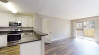 Located at 2450 Hilton Head Pl in El Cajon, CA, this single-floor residence offers a thoughtfully designed open-concept layout that seamlessly connects the kitchen and living areas. The kitchen is well-appointed with white shaker-style cabinetry, dark countertops, a peninsula with a built-in sink, and a full suite of stainless steel appliances including a refrigerator, range, and microwave. Wood-look plank flooring runs throughout the main living areas, lending warmth and continuity to the space. The living area is bright and airy, benefiting from natural light that flows in through sliding glass doors leading to an outdoor balcony. A front entry door with a decorative window further enhances the natural light in the space. Bedrooms feature neutral carpet and windows with vertical blinds. The residence includes two bathrooms: one with a sleek walk-in glass shower, white cabinetry, a square vessel-style sink, and dark countertops, and a second full bathroom with a shower-tub combination. A dedicated in-unit laundry closet with a stacked washer and dryer adds everyday convenience. The overall color palette of soft grays and whites creates a clean, modern, and inviting atmosphere throughout.