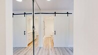 Located at 1746 N Orange Dr in the heart of Hollywood, Los Angeles, this thoughtfully designed studio offers a clean, modern aesthetic across a single-floor layout. Light wood-style luxury vinyl flooring runs throughout the entire space, creating a seamless and cohesive look that enhances the bright, airy atmosphere.

The living area is open and versatile, bathed in natural light from a wide bank of windows that frame scenic views of the surrounding Los Angeles hillside — a standout feature of this space. The combined kitchen and living room area maximizes functionality, offering an efficient, open-concept arrangement well-suited for everyday living.

Two closets provide ample storage, both appointed with sleek, modern sliding barn-style doors featuring matte black hardware — a stylish design element that adds character to the interior. The full-length mirrored door on one closet further enhances the sense of space and light.

The bathroom continues the clean, minimalist design language, featuring light wood flooring, a modern vanity with white cabinetry and brushed hardware, a glass-enclosed shower, and crisp white walls. The overall palette of white and neutral tones throughout the space creates a fresh, move-in-ready environment in one of LA's most vibrant neighborhoods.