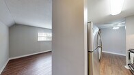Located at 1315 Morreene Rd in Durham, NC, this single-floor unit offers two bedrooms and two bathrooms within a well-organized and functional floor plan. Warm hardwood-style flooring runs throughout the living spaces and bedrooms, creating a cohesive and inviting atmosphere. Neutral gray walls complement the light-toned floors, lending the interior a clean, modern feel.

The galley-style kitchen is thoughtfully appointed with white cabinetry, dark countertops, a stainless steel range, and a full-size refrigerator, providing ample workspace and storage. Natural light filters into the bedrooms through horizontal-slatted windows, enhancing the sense of openness in each room. The spacious primary bedroom offers generous room for furnishings, while the second bedroom is equally well-sized. Both bedrooms benefit from closet storage, including a dedicated closet with a full hanging rod.

The two bathrooms feature white vanities with integrated sinks, mirrors, and textured walls. A staircase is accessible from the building exterior, which showcases characteristic brick construction. Throughout the unit, clean white trim and baseboards provide a polished finish, while ceiling vents ensure consistent climate control. This unit offers a straightforward, comfortable layout well-suited for everyday living in Durham.