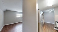 Located at 1315 Morreene Rd in Durham, NC, this single-floor unit offers two bedrooms and two bathrooms within a well-organized and functional floor plan. Warm hardwood-style flooring runs throughout the living spaces and bedrooms, creating a cohesive and inviting atmosphere. Neutral gray walls complement the light-toned floors, lending the interior a clean, modern feel.

The galley-style kitchen is thoughtfully appointed with white cabinetry, dark countertops, a stainless steel range, and a full-size refrigerator, providing ample workspace and storage. Natural light filters into the bedrooms through horizontal-slatted windows, enhancing the sense of openness in each room. The spacious primary bedroom offers generous room for furnishings, while the second bedroom is equally well-sized. Both bedrooms benefit from closet storage, including a dedicated closet with a full hanging rod.

The two bathrooms feature white vanities with integrated sinks, mirrors, and textured walls. A staircase is accessible from the building exterior, which showcases characteristic brick construction. Throughout the unit, clean white trim and baseboards provide a polished finish, while ceiling vents ensure consistent climate control. This unit offers a straightforward, comfortable layout well-suited for everyday living in Durham.