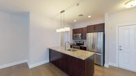 This single-floor residence offers a thoughtfully designed layout that balances open communal spaces with functional private areas. The kitchen serves as a central highlight, anchored by a substantial island with a granite countertop and integrated sink, illuminated by a modern pendant light fixture. Rich, dark-toned cabinetry lines the walls, complemented by a tile backsplash and a full suite of stainless steel appliances, including a refrigerator, range, and microwave. Wide-plank hardwood flooring extends from the kitchen into the open living and dining area, which benefits from natural light admitted through multiple windows and a sliding door dressed with vertical blinds. An elegant chandelier adds a decorative focal point to the space.

The bedrooms feature neutral carpet flooring, windows with blinds, and closets for storage. Two bathrooms are finished with light tile flooring, gray vanities with countertop sinks, mirrors, and standard fixtures, maintaining a clean and consistent aesthetic. A dedicated laundry area houses a stacked washer and dryer unit alongside a built-in countertop surface. Throughout, white trim and neutral wall tones create a cohesive, move-in-ready environment.