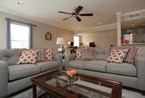 Located in Grapevine, TX, this single-story home offers a comfortable and functional layout designed for everyday living. The main living area is generously sized and anchored by light-toned wood-style flooring that runs throughout, contributing to a bright and airy atmosphere. Recessed lighting in the ceiling is complemented by a ceiling fan, ensuring the space remains well-lit and comfortable year-round. Crown molding adds a clean, finished detail along the upper walls.

The living room is arranged with a plush sectional sofa, accent chairs — including a bold patterned armchair — and a central coffee table, all positioned around a rug-defined seating zone. A wall-mounted flat-screen television serves as a focal point on one side of the room, flanked by a media console and decorative accessories. Natural light filters in through multiple windows dressed with curtains, enhancing the warm, welcoming ambiance.

A dining area with a classic wrought-iron style table and chairs occupies one corner of the space, offering a defined area for meals without sacrificing the openness of the floor plan. The layout flows intuitively, making the home feel cohesive and accessible throughout its single level.