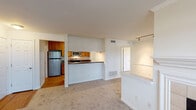 This single-floor residence offers a thoughtfully arranged layout that balances open communal spaces with comfortable private areas. The living room serves as the central gathering space, featuring neutral carpet, crown molding, a classic wood-mantled fireplace with tile surround, and multiple windows that invite natural light and views of surrounding greenery. Track lighting adds a functional accent overhead.

The kitchen is positioned adjacent to the living area, separated by a peninsula with a dark countertop that doubles as a breakfast bar. Warm wood cabinetry, dark granite-style countertops, hardwood flooring, stainless steel appliances including a refrigerator and microwave, and a louvered pantry door contribute to a practical and cohesive design.

The bedrooms are carpeted and well-lit, each featuring windows with blinds overlooking wooded views. One bedroom includes a ceiling fan with light fixture, while another offers built-in wall shelving and a baseboard heater, adding versatile storage and comfort options.

The bathroom is outfitted with a single-sink vanity featuring warm wood cabinetry and dark countertops, a large mirror, and a tiled shower-tub combination. A dedicated in-unit laundry area houses a full-size washer and dryer beneath wire shelving, providing convenient everyday functionality.