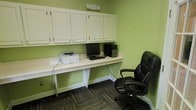 This single-floor business center is designed to provide a focused and functional workspace for productivity. The room is finished with light green walls that create a fresh, open atmosphere, complemented by patterned carpeted flooring that adds a professional touch.

A built-in, wall-length countertop workstation serves as the centerpiece of the space, offering ample surface area for work tasks. The station is equipped with a desktop computer and monitor, as well as a dedicated printer, making it a fully operational hub for computing and document needs. Overhead, a row of raised white cabinetry with paneled doors provides generous enclosed storage, keeping the workspace organized and clutter-free.

A black leather executive chair accompanies the workstation, offering comfortable seating during extended work sessions. The layout of the room is efficient and purposeful, maximizing the available space without feeling cramped. A wall-mounted air unit ensures climate comfort within the room.

Overall, this business center is well-appointed with the essential tools needed for office tasks, presenting a clean, orderly, and welcoming environment suited for guests or occupants seeking a reliable and equipped place to work.