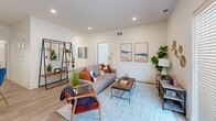 This single-story residence offers a thoughtfully organized layout across a comfortable footprint. The open-concept kitchen and living area forms the heart of the home, where the kitchen features white shaker cabinetry extending to the ceiling, a herringbone-patterned tile backsplash, stainless steel appliances including a French door refrigerator and range, and a peninsula with a undermount sink and bar seating illuminated by a modern pendant light. Light wood-style flooring flows throughout, enhancing the bright, airy atmosphere created by recessed lighting. The living area is anchored by a bold yellow front door that adds a striking design accent. A dedicated office provides a windowed, carpeted space suitable for focused work. The primary bedroom features plush carpet, a ceiling fan, and a window allowing natural light. Two full bathrooms include clean white vanities with undermount sinks and light wood flooring. A dedicated laundry room houses a full-size washer and includes a closet for additional storage. Two closets provide ample organizational space throughout. The overall aesthetic is modern and cohesive, with a clean, neutral palette accented by contemporary fixtures.