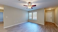 Located at 1355 Bradley Blvd in Savannah, Georgia, this single-floor residence offers a practical and well-appointed layout with a clean, neutral aesthetic throughout. The living area is bright and welcoming, featuring light-toned hardwood-style flooring, soft neutral wall colors, and a ceiling fan with integrated lighting. Natural light filters in through paired windows, creating an airy atmosphere that flows naturally through the open space.

The kitchen is a functional highlight, equipped with stainless steel appliances including a refrigerator, electric range, and over-the-range microwave. Light wood cabinetry provides ample storage, while a granite-style countertop extends to a peninsula breakfast bar that opens toward the adjacent living and dining areas. The kitchen also features its own hardwood-style flooring, maintaining a cohesive look.

The bedroom offers plush carpeting, a ceiling fan, a natural light-admitting window with vertical blinds, and a full-width closet with bifold doors, providing generous storage. The bathroom is neatly appointed with a full tub and shower combo featuring tiled surround, a wood-toned vanity, and hard surface flooring. Throughout the home, clean white trim and understated finishes contribute to a comfortable, move-in ready environment.