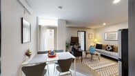 This single-floor residence offers a thoughtfully designed layout that balances comfort and functionality across several distinct living spaces. The open-plan living and dining area serves as the heart of the unit, where a dining table with modern chairs sits adjacent to a light-filled window, allowing natural light to brighten the space. The living area is anchored by a plush sofa, a patterned area rug, and a mounted television, creating a welcoming atmosphere for relaxing or entertaining.

The kitchen is efficiently arranged and equipped with stainless steel appliances, including an electric range, dishwasher, and microwave, complemented by granite-style countertops and dark cabinetry with open shelving above.

The bedrooms are carpeted and feature floor-to-ceiling vertical blind-covered windows and sliding doors that open to an outdoor area, filling each room with natural light and outdoor views. One room is configured as a flexible space with a desk and seating, suitable as a home office or additional sleeping area.

The bathroom is clean and straightforward, featuring a tub-shower combination, granite-topped vanity, and neutral finishes throughout. The overall aesthetic of the unit is modern and understated, with neutral tones and contemporary furnishings creating a cohesive, livable environment.