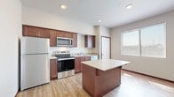 Located at 26477 72nd Ave NW, Unit 315, in Stanwood, WA, this single-floor unit offers a thoughtfully organized layout that maximizes functionality within a compact footprint. The open-concept kitchen serves as the centerpiece of the space, featuring rich dark-wood cabinetry, light stone countertops, and a full suite of stainless steel appliances including a refrigerator, electric range, and built-in microwave. A kitchen island with a clean white countertop provides additional workspace and a natural visual anchor for the open living area. Light wood-tone flooring runs throughout, lending warmth and continuity across the space. Recessed lighting and a window allowing natural light keep the area bright and welcoming. The bathroom is efficiently designed, incorporating a stacked washer and dryer unit, a vanity with matching dark-wood cabinetry, and light countertops — offering the added convenience of in-unit laundry. A connecting hallway provides smooth flow between the bathroom and the main living area. Neutral wall tones throughout the unit create a clean, versatile backdrop. Overall, this unit delivers a practical and modern living environment with efficient use of space and quality finishes.