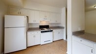This single-story residence offers a practical and well-organized layout designed for comfortable everyday living. The open living area is finished with wall-to-wall neutral carpet and features a sliding door that brings in natural light, while a half-wall partition separates the space from the adjacent kitchen. The kitchen is equipped with white cabinetry providing generous upper and lower storage, laminate countertops, a gas range, and a refrigerator, all set on durable vinyl flooring.

The bedrooms are carpeted and feature neutral walls, blinds-covered windows with views of surrounding greenery, and built-in closets with hanging rods. One bedroom includes a walk-in closet and direct access to a bathroom, which features a wide vanity with a large mirror, overhead globe lighting, and wood-toned cabinetry. A second bathroom includes tiled flooring, a shower and tub combination with teal tile surround, and a clean, functional layout. Throughout the residence, consistent neutral tones and flush-mount lighting maintain a cohesive, understated aesthetic. The floor plan, as visible in the layout scan, reflects an efficient use of space with clear separation between living, cooking, and sleeping areas.