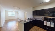 This single-floor residential unit offers a thoughtfully designed open-concept layout that seamlessly connects the kitchen and living area. The kitchen is a standout feature, showcasing dark espresso cabinetry with ample storage, granite countertops, a peninsula with breakfast bar seating, and black appliances including a refrigerator, range, microwave, and dishwasher. A fluorescent overhead light and track lighting illuminate the space effectively. Warm hardwood-style flooring flows throughout the main living areas, adding continuity and a sense of spaciousness to the open floor plan.

The living area benefits from natural light provided by a window, complemented by a ceiling fan for added comfort. Bedrooms are finished with plush carpet and ceiling fans, offering a comfortable retreat, with windows providing views of the surrounding area.

The bathroom is well-appointed, featuring a dual-sink vanity with dark cabinetry, a large mirror, and hardwood-style flooring. A separate water closet with a tub-shower combination adds functionality. A walk-in closet with built-in shelving and hanging rods provides generous storage. The neutral color palette throughout the unit creates a clean, versatile backdrop suitable for a variety of interior styles.