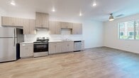Located on the third floor at 5625 S Hollywood Blvd in Las Vegas, this one-bedroom, one-bathroom unit offers a clean, modern aesthetic defined by consistent light wood-tone vinyl flooring and crisp white walls throughout. The open-concept living and kitchen area creates a generous, airy feel, with recessed lighting illuminating the space efficiently. The kitchen features a full run of light wood-grain cabinetry — both upper and lower — paired with white countertops and a complete suite of stainless steel appliances, including a refrigerator, electric range, built-in microwave, dishwasher, and range hood. The layout flows seamlessly from the kitchen into the living area, making the space feel connected and functional. The bedroom is a well-proportioned room bathed in natural light through a large window fitted with blinds, offering views of the surrounding neighborhood. A ceiling fan adds comfort to the space. The bathroom continues the unit's cohesive design language with light wood cabinetry, a white countertop vanity, a large mirror, and a tiled shower with accessibility grab bars. The hallway connecting the bathroom to the bedroom is notably spacious. Throughout, the unit presents a fresh, move-in-ready condition with a contemporary, minimalist character.
