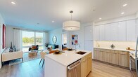 Located at 8005 Gramercy Blvd in Rockville, Maryland, this contemporary single-floor residence showcases a thoughtfully designed open-concept layout with modern finishes throughout. The kitchen serves as the heart of the home, featuring sleek two-tone cabinetry — crisp white upper cabinets paired with warm wood-toned lower cabinets — complemented by a classic subway tile backsplash, stainless steel appliances, and a generously sized island with a white quartz countertop and built-in sink. A statement drum pendant light anchors the space, which flows seamlessly into the dining and living areas. The living room is bright and welcoming, with light hardwood flooring and access to additional rooms. The bedrooms are well-proportioned and filled with natural light from large floor-to-ceiling windows that offer open views of the surrounding landscape and tree-lined streetscape. The primary bathroom features warm wood cabinetry, a white quartz vanity, light stone-look tile flooring, and direct access to a walk-in closet. A secondary bathroom provides a full tub-shower combination with coordinating tile surround and a matching wood-toned vanity. Throughout, the residence maintains a clean, modern aesthetic with a neutral palette, recessed lighting, and consistent hardwood-style flooring.
