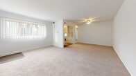 Located at 1207 Harwood Ave in Baltimore, MD, this single-floor, 2-bedroom, 1-bathroom home offers a practical and comfortable layout. The living room is a generous, open space featuring neutral carpeting, a ceiling fan with light fixture, and a large window with vertical blinds that allow natural light to fill the room. Built-in shelving is visible nearby, adding functional storage. The kitchen features light wood cabinetry, laminate countertops, hardwood-style flooring, and a full suite of white appliances including a refrigerator, stove, and washer. A window above the sink brings in additional natural light. The primary bedroom is a well-sized retreat with plush carpeting, double closets with panel doors, and clean white walls. The second bedroom also features carpet flooring and a window with vertical blinds, maintaining a bright and airy feel. Both bedrooms offer comfortable proportions suitable for furnishing. The bathroom is finished with white subway tile surrounding a full soaking tub and shower combination, accented by gold-toned fixtures, and includes a small window for ventilation. A connecting hallway ties the rooms together efficiently. Throughout, the home maintains a clean, neutral palette with white walls and light carpeting.