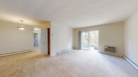 This single-floor residence offers a clean, functional layout designed for comfortable everyday living. The main living area is generously sized, featuring neutral wall-to-wall carpeting, white walls, and baseboard heating throughout. A sliding glass door opens directly onto a private balcony, allowing natural light to fill the space and providing outdoor views of surrounding greenery and the parking area below.

An adjoining dining area is illuminated by a pendant light fixture, creating a distinct yet connected space to the living room. The kitchen is outfitted with warm honey-toned wood cabinetry, white countertops, a stainless steel sink, a tile backsplash, and a window that brings in additional natural light.

The bedrooms are carpeted and feature ceiling fans with integrated lighting. One bedroom includes a built-in closet with bifold doors, offering practical storage. Each room is finished with neutral tones, contributing to a calm, cohesive ambiance throughout.

The bathroom is tiled in a classic octagonal-and-diamond pattern on both the floor and the shower surround, complemented by a white vanity with cabinet storage and a full bathtub. Wall-unit air conditioning is present in the living areas alongside the baseboard heating, ensuring year-round comfort. Overall, this residence presents a straightforward and practical living environment.