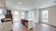 This single-floor residence features a thoughtfully designed open-concept layout that seamlessly connects the kitchen and living areas. The kitchen is a standout highlight, equipped with rich dark-wood cabinetry, granite countertops, and a full suite of stainless steel appliances, including a refrigerator, electric range, built-in microwave, and dishwasher. A central island with an undermount sink and a stylish pendant light serves as both a functional workspace and a natural gathering point. Recessed lighting and multiple windows with horizontal blinds flood the space with natural light, offering views of the surrounding neighborhood.

The open living area extends generously from the kitchen, featuring durable hardwood-style flooring and a sliding glass door providing access to an outdoor balcony. The bedrooms are carpeted for comfort; one features a wide closet with dark-wood sliding doors and a bright window, while another includes a sliding barn-style door. Two bathrooms serve the unit—one with a sleek glass-enclosed walk-in shower and chrome fixtures, and another with a full soaking tub and shower combination. The overall aesthetic is clean and contemporary, with neutral tones throughout.