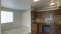 This two-floor space blends modern and industrial design elements into a cohesive living environment. The kitchen is outfitted with rich, dark wood cabinetry offering generous upper and lower storage, complemented by dark granite countertops and a classic subway tile backsplash in a soft green-gray tone. A black range anchors the cooking area, while an exposed metallic ventilation duct adds a distinctive industrial character overhead, serving as both a functional and architectural feature.

The kitchen opens directly into the living area, creating a seamless, open-concept layout that promotes an airy sense of space. The living area features neutral-toned carpeting underfoot, providing a warm contrast to the dark hardwood flooring in the kitchen. Neutral beige walls throughout maintain a clean, understated backdrop that allows the darker finishes to stand out. Recessed ceiling vents and flush-mount lighting ensure practical functionality. The overall ambiance is contemporary with industrial undertones, making for a space that balances comfort with a modern urban aesthetic across both of its floors.
