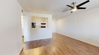 This single-story, one-bedroom, one-bathroom unit at 3055 N Flowing Wells Rd in Tucson, Arizona offers a practical and well-organized layout across a compact but functional floor plan. Warm wood-look flooring runs consistently throughout the entire space, creating a cohesive and clean aesthetic.

The open living area is bright and airy, featuring white walls, clean baseboards, and a ceiling fan with integrated lighting. A pass-through opening connects the living room to the kitchen, adding an open feel between the two spaces. The kitchen is efficiently arranged with white cabinetry extending to the ceiling, granite-look countertops, a black refrigerator, an electric range with a ventilation hood, and a utility sink — all illuminated by track lighting overhead.

The bedroom is a comfortable, well-proportioned room with a ceiling fan, natural light from a window with blinds, and direct access to two closets, providing ample storage. The bathroom features a white vanity with a granite-look countertop, a framed mirror, and a glass-door shower enclosure, all finished in a clean, neutral palette consistent with the rest of the unit.

Throughout the space, the design emphasizes simplicity and functionality, making efficient use of every square foot.