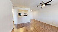 This single-story, one-bedroom, one-bathroom unit at 3055 N Flowing Wells Rd in Tucson, Arizona offers a practical and well-organized layout across a compact but functional floor plan. Warm wood-look flooring runs consistently throughout the entire space, creating a cohesive and clean aesthetic.

The open living area is bright and airy, featuring white walls, clean baseboards, and a ceiling fan with integrated lighting. A pass-through opening connects the living room to the kitchen, adding an open feel between the two spaces. The kitchen is efficiently arranged with white cabinetry extending to the ceiling, granite-look countertops, a black refrigerator, an electric range with a ventilation hood, and a utility sink — all illuminated by track lighting overhead.

The bedroom is a comfortable, well-proportioned room with a ceiling fan, natural light from a window with blinds, and direct access to two closets, providing ample storage. The bathroom features a white vanity with a granite-look countertop, a framed mirror, and a glass-door shower enclosure, all finished in a clean, neutral palette consistent with the rest of the unit.

Throughout the space, the design emphasizes simplicity and functionality, making efficient use of every square foot.