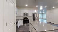 This single-floor residence presents a clean, contemporary design throughout its well-organized layout. The kitchen serves as a central highlight, outfitted with white shaker-style cabinetry, gray quartz countertops, and a full suite of stainless steel appliances including a range, microwave, refrigerator, and dishwasher. A white subway tile backsplash adds a refined touch, while pendant lighting and recessed fixtures illuminate the space. A kitchen island with additional storage provides both workspace and a natural division between the kitchen and the adjoining living area, which features wood-look flooring that extends throughout the common spaces.

The bedrooms are carpeted and bright, each benefiting from large windows fitted with horizontal blinds that allow generous natural light. One bedroom includes access to a spacious walk-in closet with dual hanging rods and carpeted flooring. Two full bathrooms serve the unit, each featuring wood-look vinyl flooring, white vanities with gray countertops, and a tub-shower combination. The overall aesthetic is consistent and modern, characterized by a neutral color palette of whites, grays, and warm beiges that creates a cohesive and inviting atmosphere throughout.