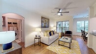 This single-story residence offers a thoughtfully designed layout with distinct living, dining, sleeping, and kitchen areas. The living room features warm hardwood flooring, crown molding, a ceiling fan, and natural light from a window overlooking greenery. A bold framed artwork anchors the space above a neutral sofa accented with navy and yellow pillows, complemented by a geometric-patterned area rug.

The adjacent dining area accommodates a full-sized table and chairs beneath track lighting, with large windows providing ample natural light and exterior views. The kitchen is equipped with rich wood cabinetry, dark granite countertops, a stone tile backsplash, and stainless steel appliances including a range and over-the-range microwave, all set over tile flooring.

Multiple bedrooms feature plush carpeting, ceiling fans, crown molding, and generous windows with exterior views. Each room is comfortably sized for a queen or larger bed with additional furniture.

The bathrooms include tiled tub-shower combinations, white cabinetry with built-in storage, and granite-topped vanities, maintaining a clean, functional aesthetic consistent throughout the home.