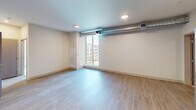 This 690-square-foot, two-bedroom apartment is located in Pittsburgh, PA 15201, and offers a well-organized single-floor layout designed for efficient urban living. The kitchen is a standout feature, outfitted with dark espresso cabinetry, light countertops, and a full suite of stainless steel appliances including a French door refrigerator with ice and water dispenser, a range, microwave, and dishwasher. Light wood-style flooring runs throughout the main living and kitchen areas, contributing to a clean, contemporary aesthetic complemented by recessed lighting. An exposed ductwork element in the living area adds an industrial design touch, while large floor-to-ceiling windows flood the space with natural light and provide views of the surrounding urban development. The primary bedroom measures 160 square feet and features plush carpeting, a closet with built-in shelving, and generous wall space. The second bedroom is similarly carpeted, featuring a large window with abundant natural light and views of the cityscape. Both bedrooms offer a neutral color palette with beige tones, creating a calm and functional environment. The apartment's overall layout, as seen in the 3D overview, reflects a compact but thoughtfully designed floor plan suited for urban residential living.