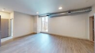 This 690-square-foot, two-bedroom apartment is located in Pittsburgh, PA 15201, and offers a well-organized single-floor layout designed for efficient urban living. The kitchen is a standout feature, outfitted with dark espresso cabinetry, light countertops, and a full suite of stainless steel appliances including a French door refrigerator with ice and water dispenser, a range, microwave, and dishwasher. Light wood-style flooring runs throughout the main living and kitchen areas, contributing to a clean, contemporary aesthetic complemented by recessed lighting. An exposed ductwork element in the living area adds an industrial design touch, while large floor-to-ceiling windows flood the space with natural light and provide views of the surrounding urban development. The primary bedroom measures 160 square feet and features plush carpeting, a closet with built-in shelving, and generous wall space. The second bedroom is similarly carpeted, featuring a large window with abundant natural light and views of the cityscape. Both bedrooms offer a neutral color palette with beige tones, creating a calm and functional environment. The apartment's overall layout, as seen in the 3D overview, reflects a compact but thoughtfully designed floor plan suited for urban residential living.