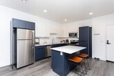 Located at 2640 W 3800 S in West Valley City, Utah, this thoughtfully designed one-bedroom, one-bathroom residence offers a contemporary living experience across a single well-organized floor. The open-concept layout seamlessly connects the kitchen and living room, maximizing the efficient use of space.

The kitchen is a standout feature, showcasing a striking two-tone design with navy blue lower cabinetry contrasted against crisp white upper cabinets. A large central island with a white quartz countertop provides seating for two and serves as an ideal prep and gathering space. Stainless steel appliances, including a refrigerator, dishwasher, microwave, and range, complete this functional and stylish kitchen.

The living room is bright and welcoming, with large sliding glass doors that open to a private balcony, flooding the space with natural light and offering outdoor views. Light wood-style flooring runs throughout the main living areas, adding warmth to the modern aesthetic.

The bedroom is a comfortable retreat, featuring large windows with sheer curtains that allow ample natural light, plush carpeting, and ample wall space. The bathroom continues the navy and white design theme with a matching vanity, light wood-style flooring, and a shower-tub combination. Recessed lighting throughout enhances the clean, modern ambiance of the entire home.