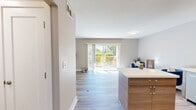 This 510-square-foot, single-floor apartment on La Selva Street in San Mateo offers a well-designed 2-bedroom, 1-bathroom layout that maximizes every inch of available space. The combined kitchen and living area serves as the heart of the home, showcasing a contemporary kitchen with two-tone cabinetry in white and warm wood tones, a patterned tile backsplash, open wooden shelving, stainless steel appliances including a refrigerator, range, microwave, and dishwasher, and a central island with a white countertop providing additional workspace. Light wood-style flooring runs throughout, complementing the neutral wall tones and creating a cohesive, modern aesthetic. The living area is bathed in natural light through large sliding glass doors that open to a private balcony with views of lush greenery. The primary bedroom measures 130 square feet and features a sliding-door closet, while the second bedroom benefits from a large window with outdoor views. The full bathroom includes a soaking tub with tiled surround and a clean, minimalist finish. A hallway connects all rooms efficiently, completing this smartly laid-out apartment.