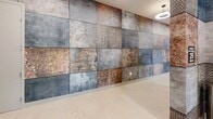 This 1,660-square-foot fitness center in Charlotte, NC (28206) is a thoughtfully designed, single-floor facility spread across two open workout areas. The space features durable speckled carpet and hard flooring, recessed ceiling lighting, and large windows that allow natural light to fill the training floor, creating a bright and energizing environment. Overhead, stylish large-blade ceiling fans provide airflow throughout the space.

A defining architectural element is the bold accent wall clad in large-format mixed-texture tiles, combining concrete, rust, and perforated metal finishes in a grid pattern that gives the gym a modern industrial aesthetic. Full-length mirrors are strategically positioned to maximize perceived space and support proper form during workouts.

The strength training area is stocked with a multi-functional cable machine, a heavy punching bag, free weights, weight benches, and a functional trainer with battle ropes and resistance accessories. A dedicated cardio section houses treadmills, stationary bikes, and rowing machines aligned along the windowed wall. The layout ensures ample floor space between equipment for safe, comfortable movement. Together, the two zones provide a comprehensive fitness experience suitable for a wide range of training styles and goals.