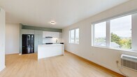 Located at 3260 SE Milwaukie Ave in Portland, OR, this thoughtfully designed two-bedroom, one-bathroom unit offers a clean, modern aesthetic across a single floor. Light wood flooring runs throughout, tying together a cohesive and bright interior. The open-concept kitchen and living area serves as the heart of the home, featuring flat-front cabinetry in soft sage and white tones, white subway tile backsplash, a stainless steel sink with a matte black faucet, and a spacious white quartz peninsula ideal for dining or meal prep. Full-size appliances, including a black refrigerator and range, complete the kitchen. Large windows in the living area invite generous natural light and offer views of the surrounding Portland neighborhood and tree canopy. Both bedrooms are well-proportioned, bright, and equipped with individual climate control units. The primary bedroom includes a dedicated closet, while the second bedroom also benefits from a window with outdoor views. The full bathroom is finished with vertical white tile surrounding a soaking tub and shower, matte black fixtures, a vanity with drawer storage, and warm wood-tone flooring. The overall ambiance is fresh, minimal, and move-in ready.