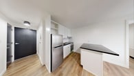 This studio apartment at 111 Porter Ave in Buffalo, NY offers a clean, modern design across a single floor. The open layout maximizes functionality, with warm hardwood-style flooring flowing seamlessly throughout the space, creating a cohesive and inviting atmosphere.

The kitchen is a standout feature, outfitted with crisp white cabinetry, a stainless steel refrigerator, an electric range with oven, an under-cabinet range hood, and a tile backsplash. A peninsula island with a dark countertop provides additional prep space and serves as a natural division between the kitchen and the main living area, adding both utility and a contemporary visual contrast.

The living area is bright and open, benefiting from natural light admitted through windows fitted with blinds. A wall-mounted thermostat and a through-wall HVAC unit ensure year-round climate control. The clean white walls and uncluttered design lend the space a fresh, move-in-ready appeal.

The unit also includes a dedicated sleeping or flex area, finished with the same light flooring and neutral white walls, offering versatility for use as a bedroom or home office. The dark front entry door adds a bold design accent upon entry. Overall, the unit presents a minimalist, well-appointed living space suited to modern urban living in the heart of Buffalo.