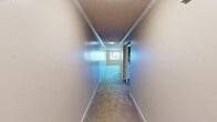 This single-story unit in Slidell, Louisiana, offers a practical and efficient layout across a modest footprint. The interior is defined by neutral beige tones, textured ceilings, and white trim throughout, creating a clean, consistent aesthetic. Hardwood-style flooring runs through the main living and kitchen areas, while plush carpet covers both bedrooms.

The combined kitchen and living area forms the heart of the unit. The kitchen features warm wood cabinetry, granite-style countertops, a breakfast bar peninsula, and white appliances including a range, built-in microwave, and refrigerator. A ceiling fan with a light fixture adds functionality to the adjacent living space.

A central hallway connects the main living area to the bedrooms and bathroom, lined with textured walls and crown molding. The primary bedroom offers a comfortable amount of space, with a window fitted with vertical blinds and access to an additional room or closet through a sliding door. The second bedroom is similarly appointed, featuring carpet flooring, a window, and textured ceiling. The bathroom includes wood-toned cabinetry, wood-style flooring, and clean, simple finishes throughout.