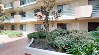 This multi-story building is centered around a well-maintained open-air courtyard that serves as the architectural focal point of the property. The courtyard is paved with warm terra cotta clay tiles that extend throughout the walkways, creating a cohesive and inviting atmosphere. A tiered decorative stone fountain enclosed by a curved iron railing stands prominently in the courtyard, adding a classical, elegant touch to the outdoor common area.

Raised concrete planters throughout the courtyard are filled with a diverse array of mature plantings, including magnolia trees, sago palms, tropical foliage, and neatly trimmed shrubs, providing year-round greenery and visual interest. The building's exterior features a neutral stucco finish accented by pink tile cladding on pilasters and column faces, with green metal railings lining the open-air corridors on upper levels.

Ground-floor units are accessed directly from the courtyard via individual white entry doors, each with large windows allowing natural light. Upper-level balconies overlook the courtyard below. A mailbox station is conveniently located within the shared courtyard space. The open-air design allows abundant natural light to fill the common areas throughout the day.
