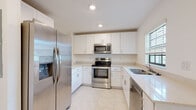 Located at 2101 E Landings Way in Port Charlotte, Florida, this two-story home offers a clean, modern aesthetic throughout its well-designed layout. The kitchen is a functional centerpiece, featuring crisp white shaker cabinetry, light quartz countertops, and a full suite of stainless steel appliances including a French door refrigerator with ice maker, electric range, over-the-range microwave, and dishwasher. Light-toned porcelain tile flooring extends through the main living areas, enhancing the bright and airy feel. A spacious living area on the ground floor features a sliding glass door that opens to an outdoor view of lush green surroundings, flooding the room with natural light. A half bathroom on the lower level provides added convenience. The staircase leads to the upper floor, where carpeted bedrooms offer a comfortable retreat, each equipped with built-in closets featuring bifold doors and windows that allow for natural light. The bathrooms are finished with neutral beige tile surrounds in the tub/shower combinations, white vanities, and tile flooring, maintaining a cohesive and clean design throughout. The overall ambiance of the home is light, neutral, and move-in ready, suited for the sunny Florida lifestyle.