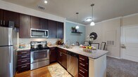 This single-floor residence offers a thoughtfully designed layout with a seamless flow between its key living spaces. The kitchen is a standout feature, showcasing rich dark-wood cabinetry, granite countertops, and a full suite of stainless steel appliances including a range, microwave, refrigerator, and dishwasher. A peninsula with additional counter space and pendant lighting connects the kitchen to a dedicated dining area, making it ideal for both everyday meals and entertaining. Crown molding adds a refined touch throughout.

The living room is generously proportioned, featuring crown molding, a ceiling fan, and a sliding glass door that opens to a private balcony with outdoor seating. The space is bright and inviting, with warm neutral tones and plush carpeting underfoot.

The primary bedroom offers a serene retreat with a bold accent wall, ceiling fan, and ample room for a full furniture arrangement. Additional bedrooms provide flexible use, including one configured for bunk beds. Both bathrooms are finished consistently with dark vanity cabinetry, granite countertops, and tub-shower combinations with tile surrounds, complemented by hardwood-style flooring. A dedicated in-unit laundry closet with stacked washer and dryer adds everyday convenience to this well-rounded residence.