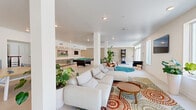 Located at 3262 30th Ave S in Saint Petersburg, Florida, this single-floor community amenity space offers a generously sized, open-plan layout designed for recreation and social gathering. The interior is defined by a clean, contemporary aesthetic, with large-format white tile flooring, bright white walls, and structural columns that subtly delineate different activity zones without compromising the open feel of the space.

The lounge area is anchored by a large sectional sofa in light gray, paired with a mid-century modern wood coffee table and set atop a bold, floral-patterned area rug. A circular teal accent rug nearby hosts a pair of sculptural lounge chairs, adding a stylish focal point to the central zone. Lush tropical plants, including monstera and bird-of-paradise, are strategically placed throughout, contributing a fresh, Florida-inspired ambiance.

Toward the rear, a dedicated game room features a full-size pool table, a built-in wet bar with stainless steel appliances and modern cabinetry, a wall-mounted television, and an arcade-style dart machine. A separate seating nook with rattan chairs and a wall-mounted TV provides a quieter retreat. Multiple windows along the perimeter allow natural light to flood the interior, with views of the surrounding outdoor areas.