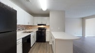 Located at 1110 Garden Walk Blvd in Atlanta, GA, this single-floor residence offers a well-organized layout designed for comfortable everyday living. The open living and dining area is finished with durable wood-look flooring and neutral gray walls, creating a clean, contemporary feel. A large sliding glass door floods the space with natural light while providing views of the outdoors, complemented by vertical blinds for privacy. A ceiling-mounted light fixture anchors the dining area.

The kitchen is efficiently designed with white cabinetry, a mosaic tile backsplash, and light-toned countertops. Black appliances — including a refrigerator, electric range, dishwasher, and under-cabinet range hood — provide a bold contrast to the bright cabinetry. A peninsula counter with a curved edge extends into the living space, offering additional prep or seating space and creating a natural boundary between the kitchen and main living area.

The bedrooms feature plush carpeting, neutral walls, textured ceilings, and windows that invite natural light. Each bedroom includes closet access. The bathroom is neatly appointed with a tiled tub-and-shower combination, a light countertop vanity, and wood-look flooring that ties back to the rest of the home's consistent design palette.